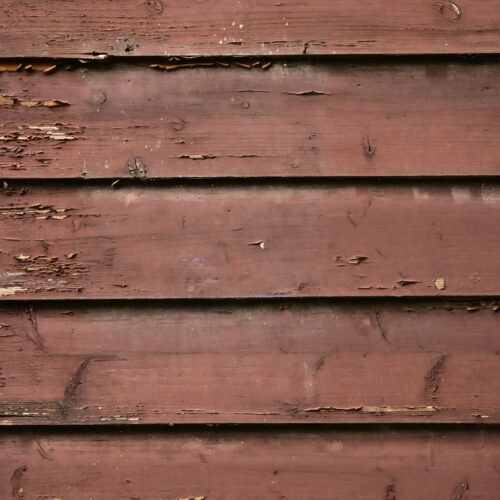 pixta_111631778_M - 堀岡美装店 Weathered brown wooden siding with peeling paint and rough surface texture.