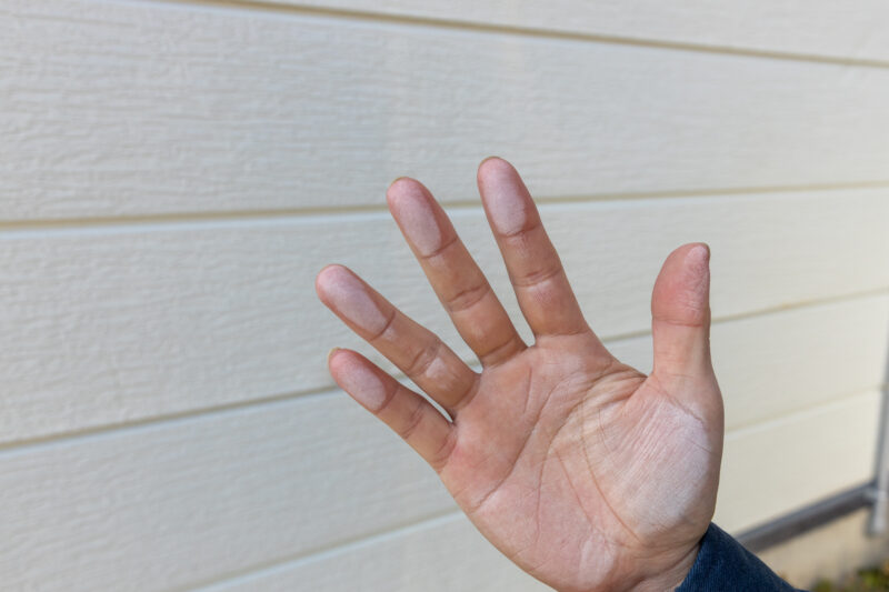 pixta_124534980_M - 堀岡美装店 Hand with white chalk dust on fingertips, fingers spread, against a pale wooden wall background.