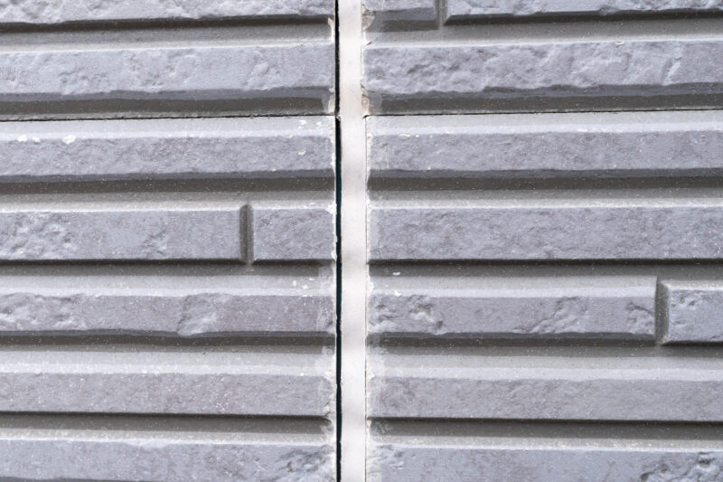 pixta_136780868_M - 堀岡美装店 Gray brick wall close-up with a prominent vertical seam in the center and textured, grooved blocks on both sides