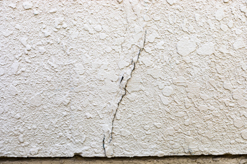 pixta_90583967_M - 堀岡美装店 Beige textured wall with a prominent vertical crack running down the center and a dark base at the bottom edge.
