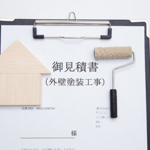 Clipboard with a Japanese quotation form (御見積書) and a small wooden house model plus a paint roller laid on top, symbolizing a home exterior painting quote.